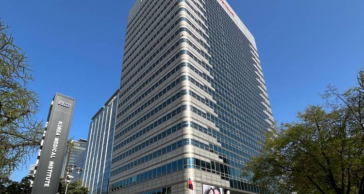 Grande tour de bureaux moderne sous un ciel bleu dégagé avec une pancarte indiquant « Korea Medical Institute » au premier plan.
