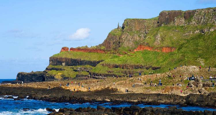 Les colonnes de basalte et les falaises vertes de la côte de la Chaussée des Géants parsemées de visiteurs par une belle journée ensoleillée.