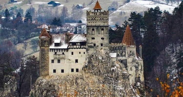Le château de Bran emblématique, perché sur une falaise rocheuse couverte de neige, se dresse sur fond de forêt.