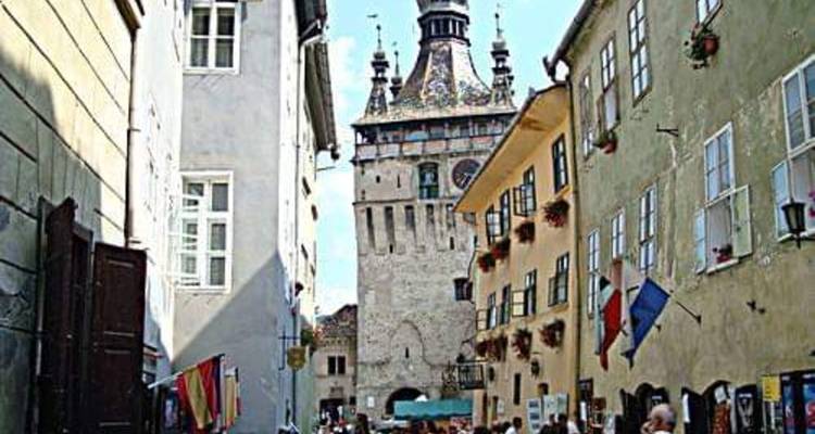 Smalle middeleeuwse steeg in Sighisoara die naar de klokkentoren leidt, omzoomd met vlaggen en cafés.