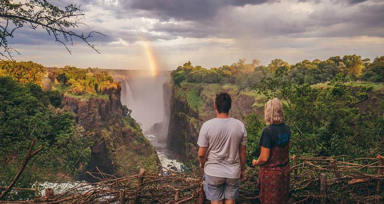 Los viajeros admiran las Cataratas Victoria y el arco iris desde un mirador escénico al atardecer