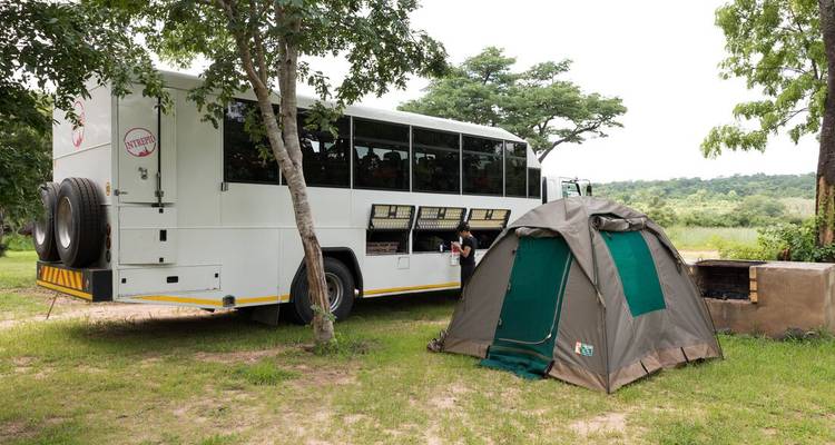 Camión de expedición terrestre estacionado junto a una carpa domo montada en un campamento en terreno con pasto.