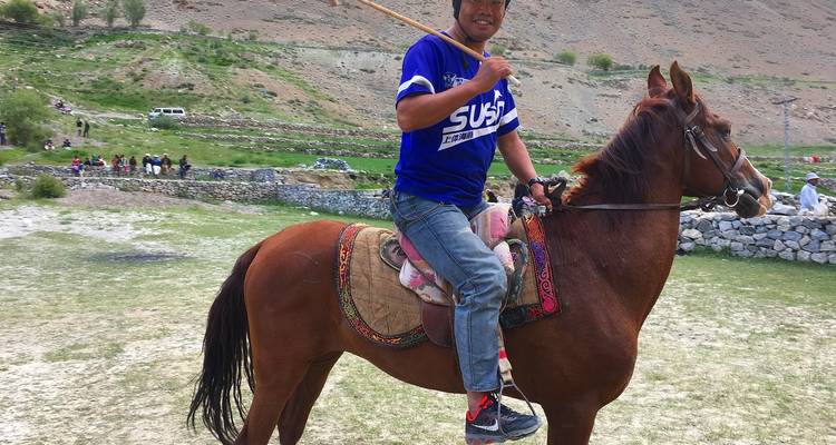 Un jeune homme à cheval, sellé et tenant un maillet de polo, dans une vallée de montagne pakistanaise.