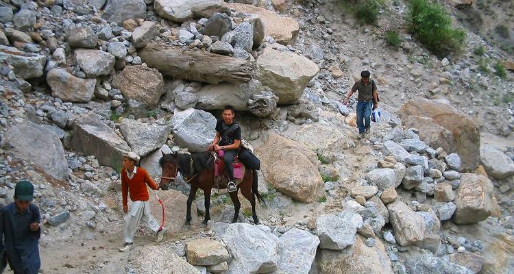 Des villageois locaux et un enfant sur un poney naviguant sur un sentier de montagne rocailleux avec des rochers tout autour.