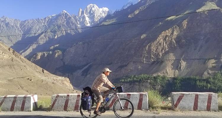 Fietser op beladen toerfiets op de Karakoram Highway met dramatische sneeuwtoppen op de achtergrond