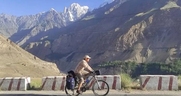 Fietser op bergweg met hoge scherpe pieken op de achtergrond, licht bijgesneden versie