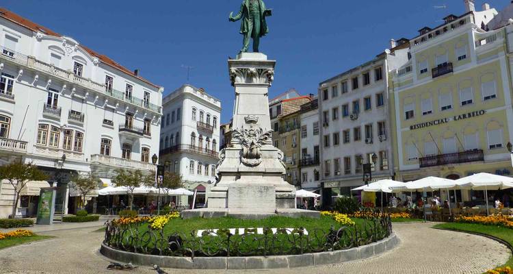 La place centrale de Coimbra présente une statue entourée de bâtiments historiques blancs et de terrasses de café.