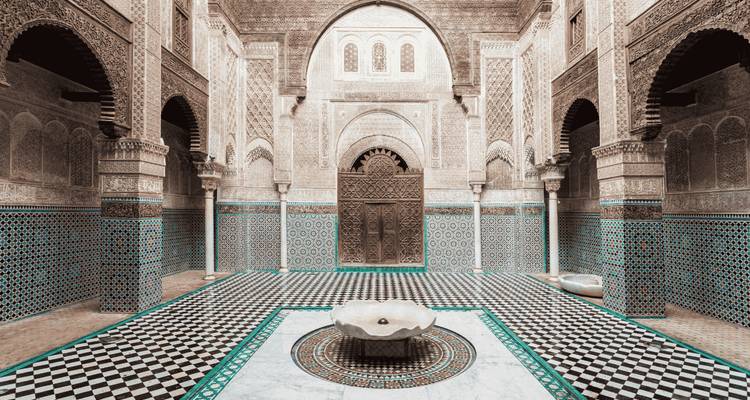 Cour de madrasa somptueusement carrelée avec des arcs en cèdre sculpté, une fontaine en marbre et des mosaïques géométriques.