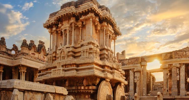 Le char en pierre emblématique du temple de Vittala à Hampi est baigné dans la lumière dorée du petit matin contre un ciel dramatique.