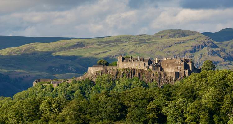 Le château de Stirling s'élève majestueusement au sommet d'un rocher boisé face à des collines verdoyantes ondulantes.