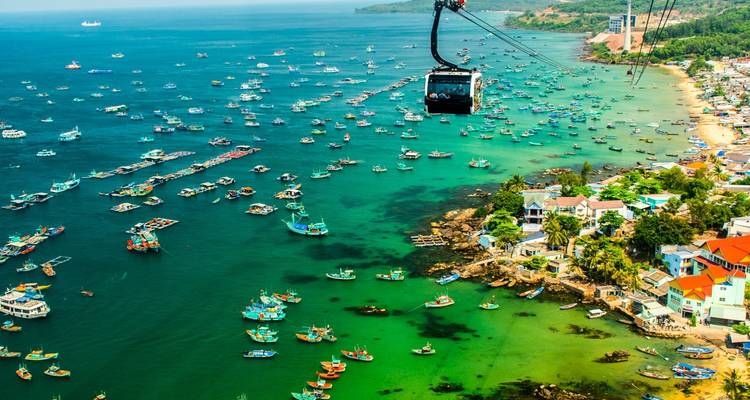 Aerial of turquoise Phu Quoc coast dotted with fishing boats beneath a cable-car gondola