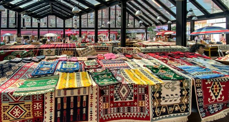 Overdekte bazaar vol kleurrijke geweven tapijten en textiel op kramen onder een glazen dak.