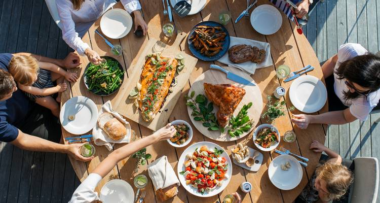 Bovenaanzicht van een houten tafel vol met heerlijke gerechten om te delen, terwijl een groep samen eet.
