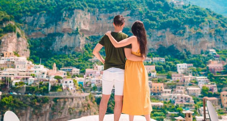 Un jeune couple s'embrassant en admirant les maisons pastel de Positano construites sur des falaises côtières escarpées.