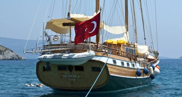 Achterdek van een houten gulet met de Turkse vlag, afgemeerd in blauw water.