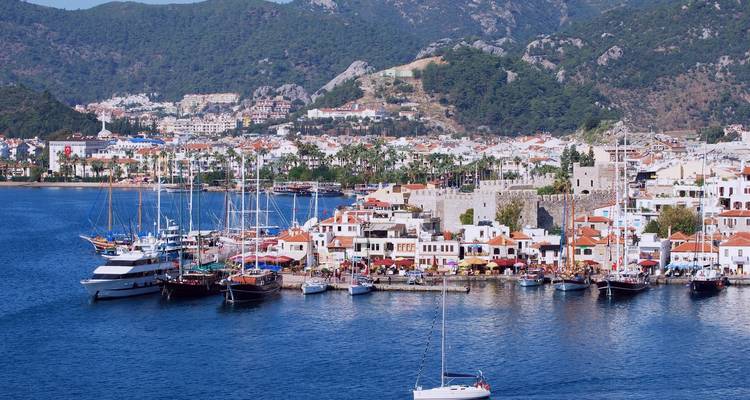 Haven van Marmaris met stenen kasteel, kleurrijke waterkantgebouwen en jachten tegen beboste bergen.