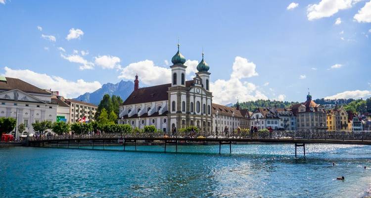 Église baroque jésuite et pont historique enjambant le lac turquoise de Lucerne.