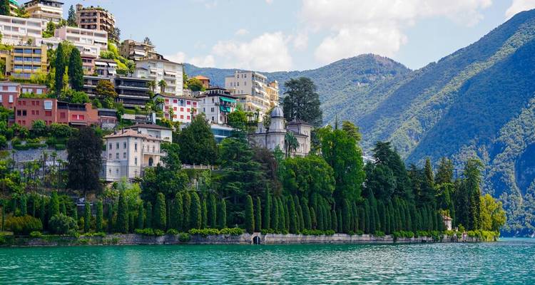 Des villas élégantes et des cyprès luxuriants bordent un lac alpin tranquille dominé par des collines boisées.