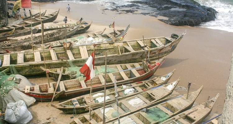 Des bateaux de pêche traditionnels en bois alignés sur une plage de sable à côté d'un littoral rocheux.