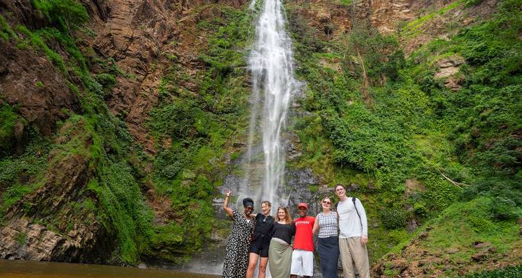 Petit groupe de voyageurs posant devant une haute cascade à un bassin rocheux.