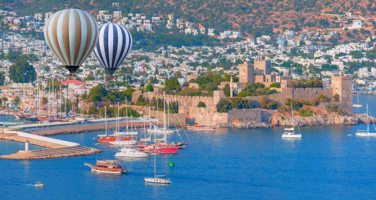 Kleurrijke luchtballonnen zweven op een zonnige dag boven het kasteel en de jachthaven van Bodrum.