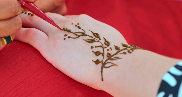 Un artiste applique des motifs de henné délicats sur le dos d'une main sur un fond de tissu rouge.