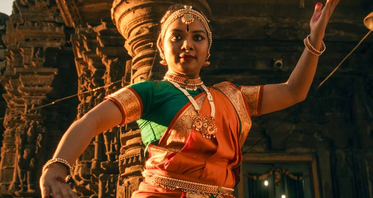 Danseur traditionnel vêtu d'un costume en soie éclatant se produit avec grâce parmi les piliers de pierre anciens au crépuscule.