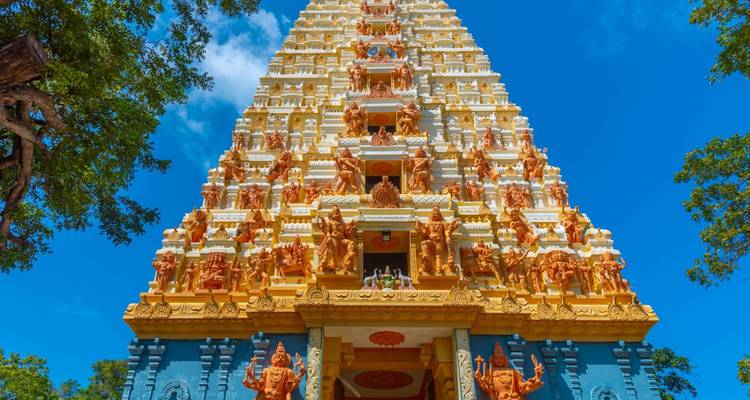 Un gopuram de temple hindou coloré, richement sculpté de divinités, s'élève contre un ciel bleu profond.