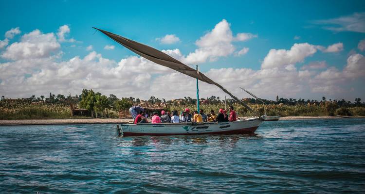 Une felouque traditionnelle avec des touristes glisse sur le Nil sous une voile latine qui ondule.