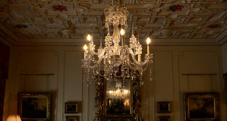 Un lustre en cristal brillant dans un salon historique orné avec un plafond sculpté.