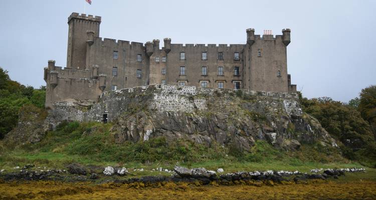Forteresse de pierre perchée sur un monticule rocheux au-dessus d'une côte parsemée d'algues par un jour gris.