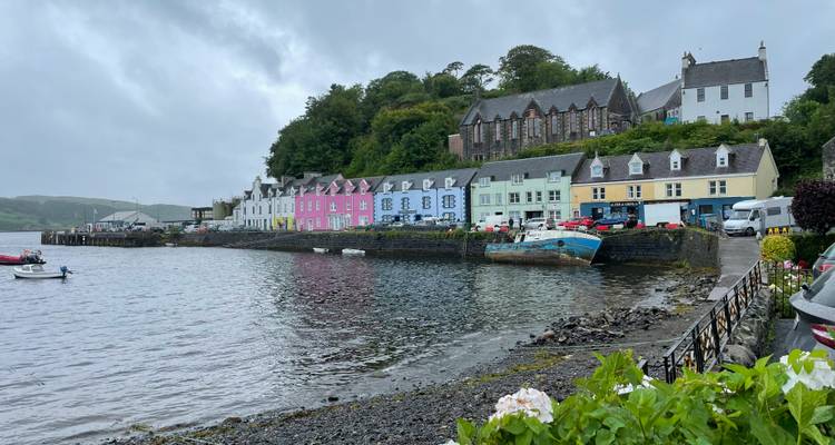 Rangée colorée de maisons en front de mer à Portree reflétées dans une baie abritée sous un ciel brumeux.