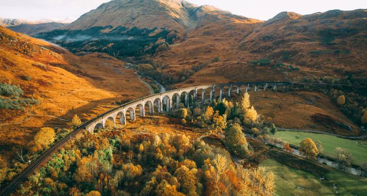 Vue aérienne automnale du viaduc de Glenfinnan qui serpente à travers le paysage des highlands doré.