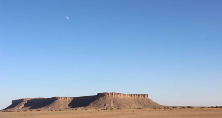 Une mesa aux sommets aplatis s'élevant du désert aride sous un ciel dégagé avec une lune visible.