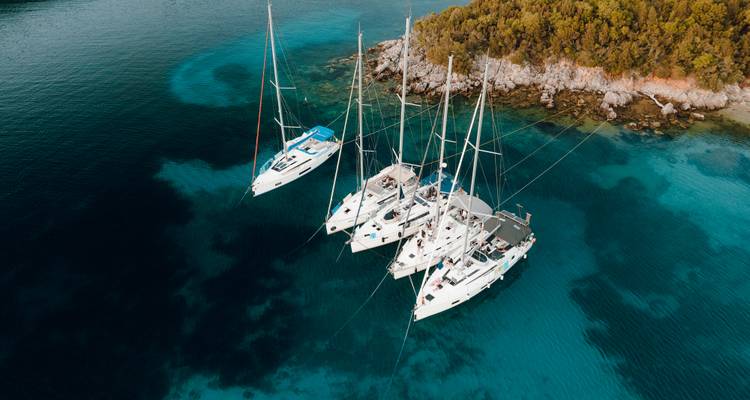 Vue aérienne de quatre catamarans amarrés ensemble dans des eaux turquoise cristallines à côté d'une petite île couverte de pins.