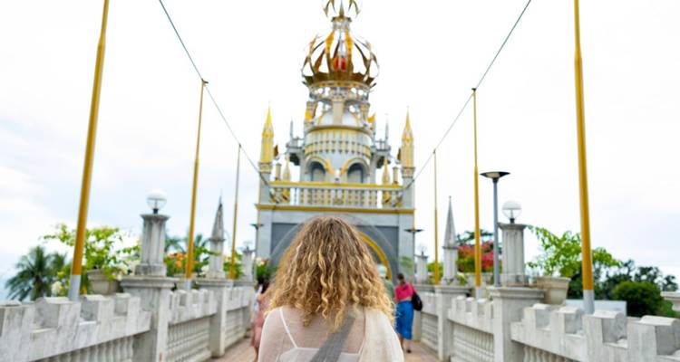 Rückansicht eines Reisenden, der sich an einem bewölkten Tag auf einen verziert gestalteten philippinischen Tempel mit goldenen Spitzen zubeweg.