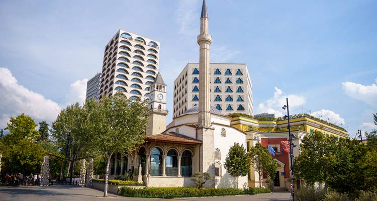 Mosquée historique et tour de l'horloge encadrées par des immeubles de grande hauteur modernes dans une place de la ville.