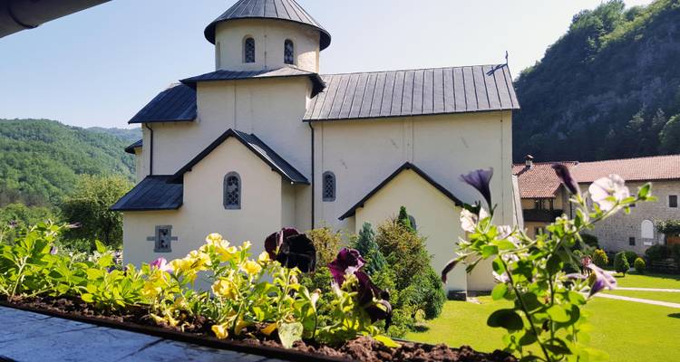 Elfenbeinfarbenes Kloster mit kreisförmiger Apsis und Schieferdach in einem üppigen Bergtalgarten