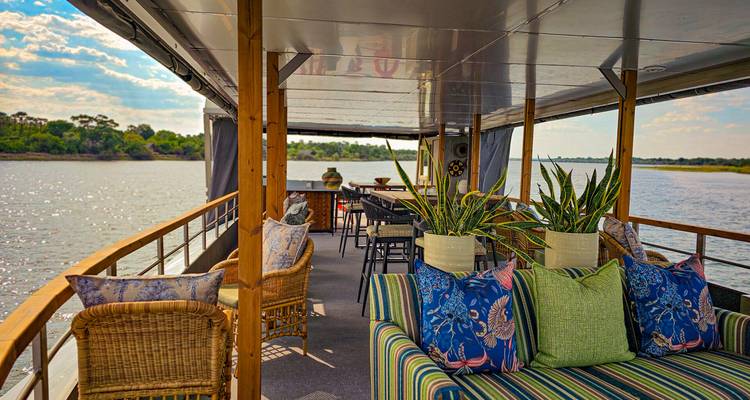 Cubierta de salón cómoda en barco fluvial con cojines estampados y vista al río