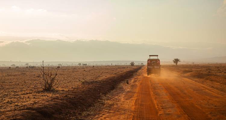 Vehículo de safari bajando por un polvoriento sendero naranja a través de una vasta llanura al atardecer