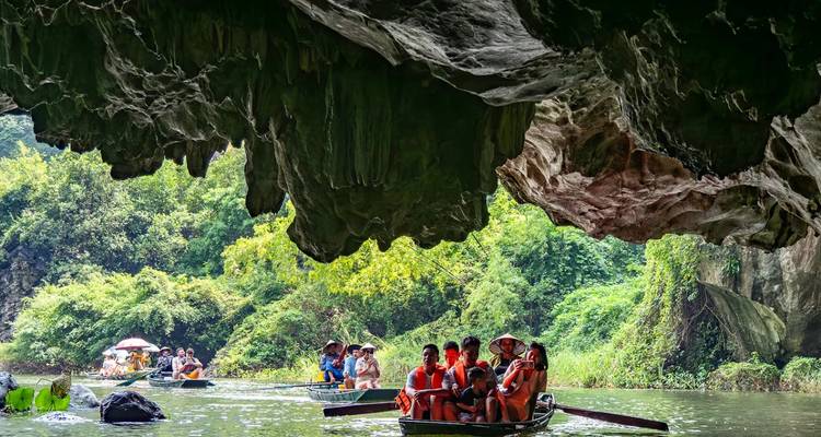 Rowboats glide through a dramatic limestone cave opening onto lush river landscapes in Ninh Binh.