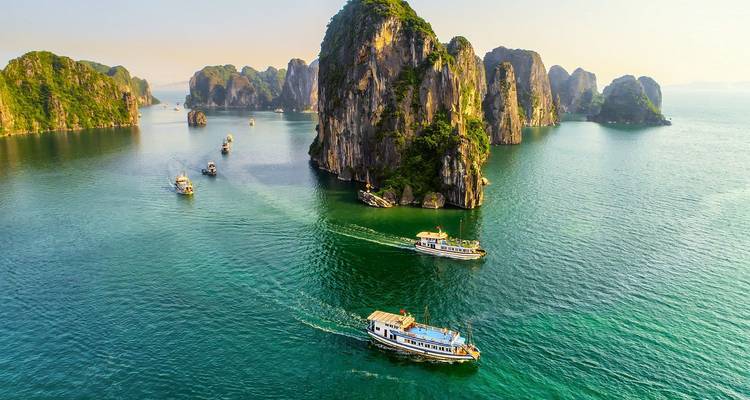Aerial view of cruise boats sailing among towering limestone islands in turquoise waters.