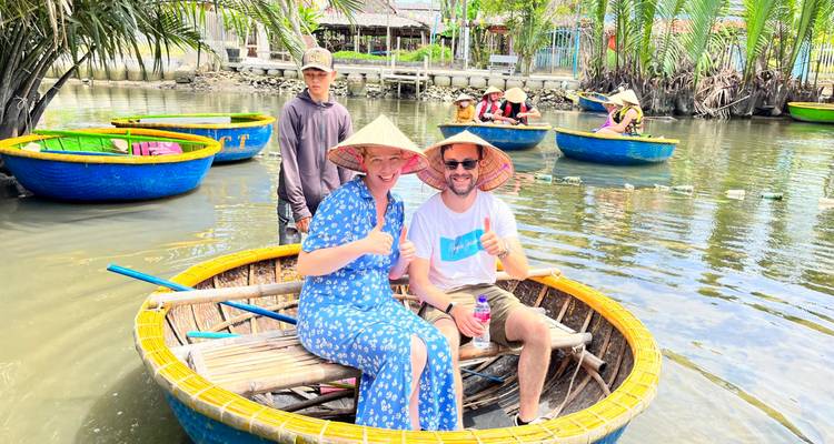 Smiling couple and boatman sit inside a round bamboo basket boat on a calm pond with other boats behind.