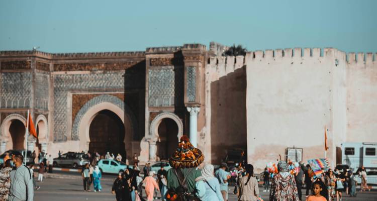 Menschenmengen gehen unter dem kunstvollen gekachelten Tor der historischen Medina von Meknes hindurch.