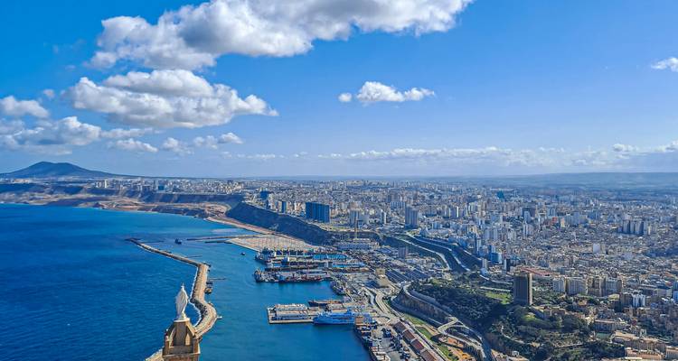 Vue panoramique aérienne de la côte d'Oran, des installations portuaires et de l'étendue urbaine sous un ciel bleu.