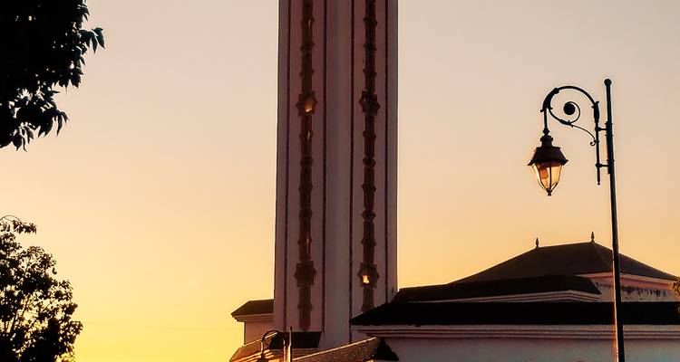 Silhouette d'un minaret et d'un lampadaire vintage contre un ciel au coucher de soleil orange.