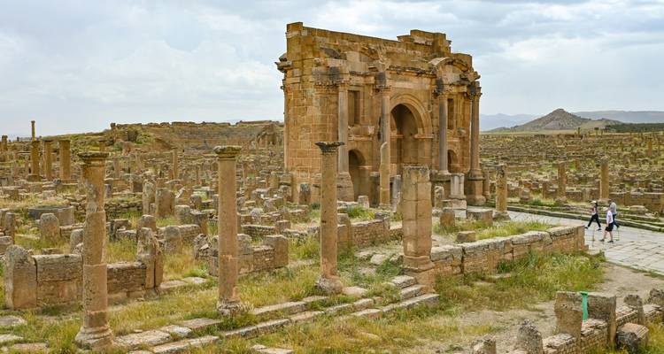 Des ruines romaines étendues avec un arc de triomphe bien conservé s'élevant au milieu de colonnes brisées à Timgad.