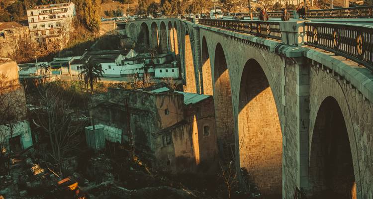 Long viaduc en pierre à plusieurs arches baigné dans la lumière de fin d'après-midi au-dessus d'une ville.
