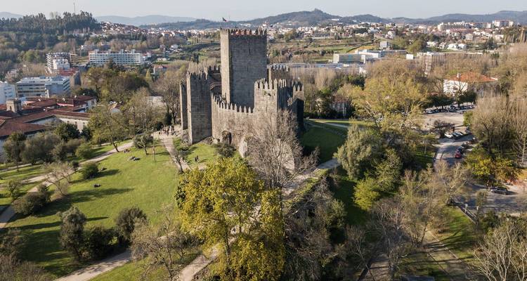 Vue aérienne du château médiéval de Guimarães entouré d'arbres et de banlieues de la ville.
