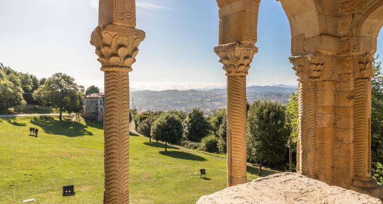 Columnas de piedra prerrománicas se alzan sobre verdes colinas ondulantes y una ciudad lejana desde una colina cerca de Oviedo.